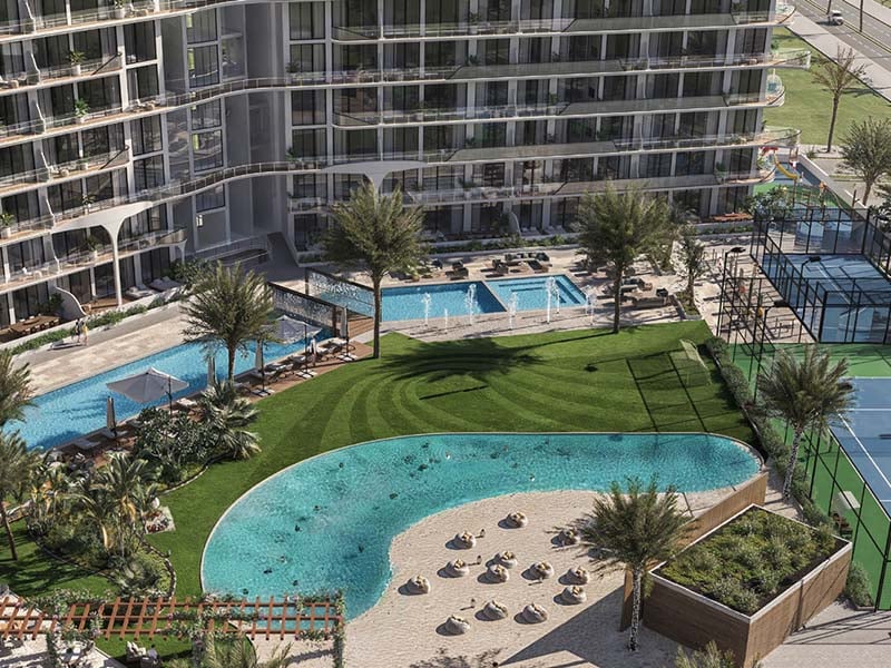 Hammock Park by Divine One brings Miami Beach flair to Wasl Gate, Dubai. This residential project blends stylish interiors with resort-like amenities in a vibrant urban setting. Inside, studios and one to two-bedroom apartments showcase thoughtful design. Living spaces flow seamlessly, bathed in natural light. Kitchens feature islands, soft-close drawers and German appliances. Bathrooms boast rain showers and Bagno Design fittings. Private balconies extend living areas outdoors, offering community views. Smart home features and track lighting allow residents to tailor their environment. Warm floors, eco-conscious materials and energy-efficient systems blend comfort with sustainability. Fully furnished options provide move-in ready homes. Beyond the apartments, Hammock Park offers a world of leisure. A sandy lagoon and swimming pools invite relaxation. Sports enthusiasts can enjoy tennis, basketball and padel courts. An outdoor beach cinema and BBQ areas foster community connections. For tranquility, a Zen yoga garden provides a peaceful retreat. The top floor houses the Elevate Hub, featuring a co-working space, gaming zone, gym, sauna and steam room. Solar-paneled pergolas showcase the project's green commitment.